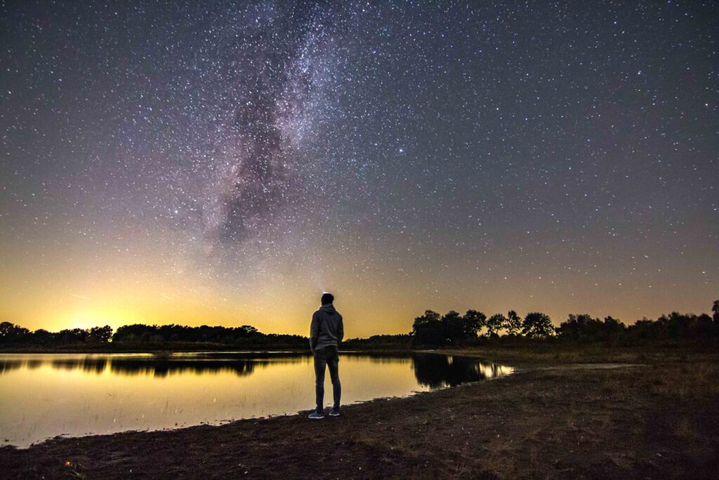 man-standing-lakeshore-against-star-field-night
